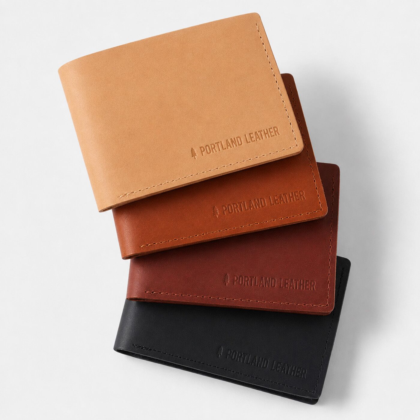 Naturale | Four leather bifold wallets stacked diagonally on a light gray background, each embossed with 'PORTLAND LEATHER'.