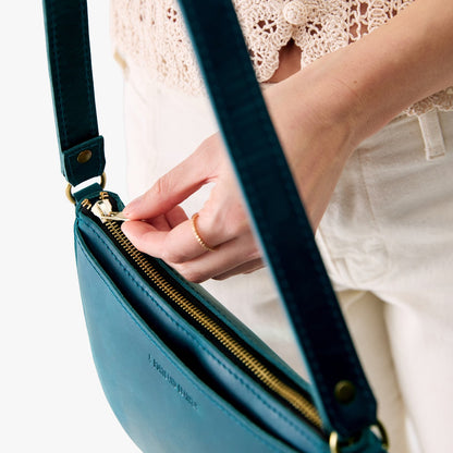Westward Blue*Small | Model holding petite bean shaped shoulder bag with a zipper closure