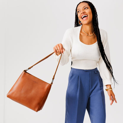 Honey*Classic | Model holding leather triangular shoulder bag with zipper top closure and wide shoulder strap