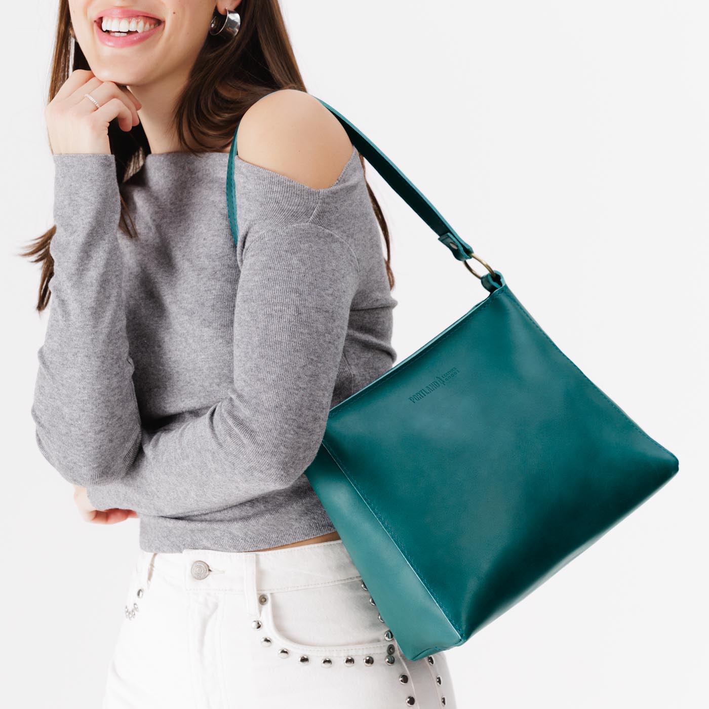 Caribbean*Small | Model carrying leather triangular shoulder bag with zipper top closure and wide shoulder strap