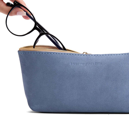 Denim | Model hand pulling pair of glasses from leather utility bag pouch with top zipper