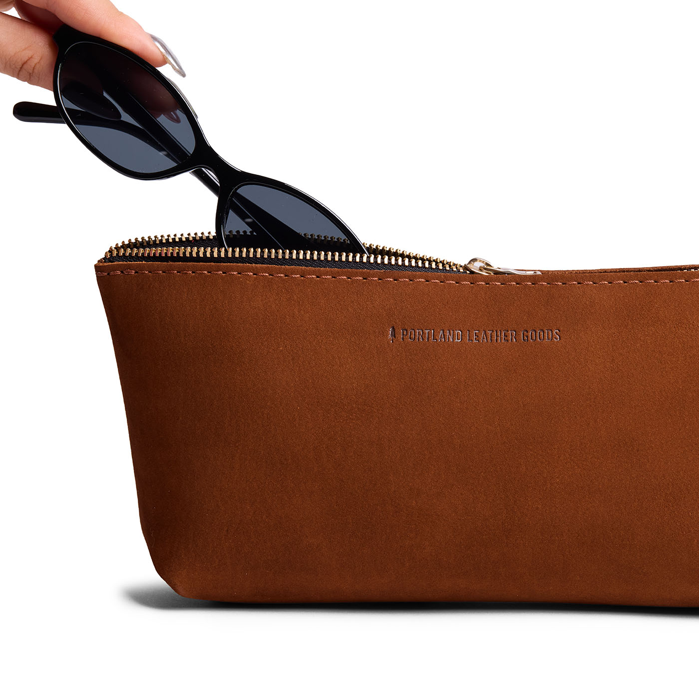 Wildwood | Model hand pulling pair of sunglasses from leather utility bag pouch with top zipper